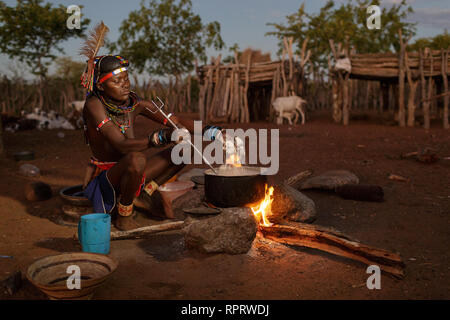 Belle jeune femme de la tribu Zemba en costume traditionnel dîner cuisiniers sur un feu en plein air dans la soirée, la Namibie, l'Afrique Banque D'Images