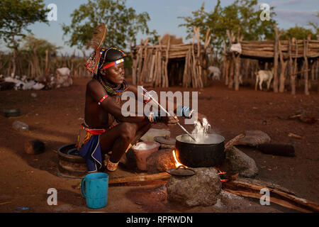 Belle jeune femme de la tribu Zemba en costume traditionnel dîner cuisiniers sur un feu en plein air dans la soirée, la Namibie, l'Afrique Banque D'Images