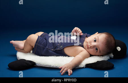 Bébé garçon couché sur un oreiller en bleu fond studio Banque D'Images