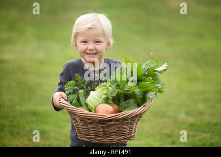 Un enfant blond heureusement montre sa récolte de fruits et légumes Banque D'Images