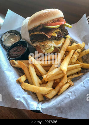 Burger à forte teneur en calories avec frites, sauce bbq et ranch dans une assiette sur une table en bois à l'intérieur d'un restaurant. Vue de dessus Banque D'Images