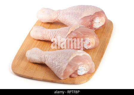 Trois pilons de poulet crus sur un boardn à découper en bois isolé sur fond blanc Banque D'Images