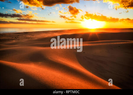 Rayons de soleil sur l'horizon au coucher du soleil dans les dunes de sable du désert aride de Stockton Beach sur la côte du Pacifique de l'Australie avec la lumière du soleil chaude casting nuances entre s Banque D'Images