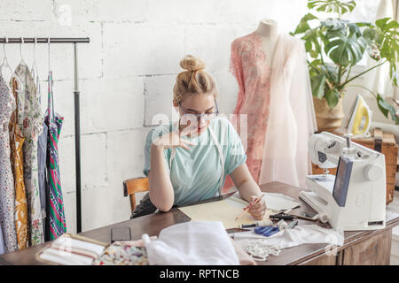 Créateur de mode sur mesure Belle de mesure se situe à dessin en milieu de travail ou de mettre par écrit les résultats après la mesure. Son studio est ensoleillée, pleine de colorf Banque D'Images