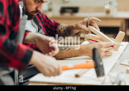 Young caucasian père et son fils pré-ado qui travaillent ensemble dans un atelier en bois, la construction d'une maison d'oiseau en bois. Petit garçon habillé en tablier et weari Banque D'Images