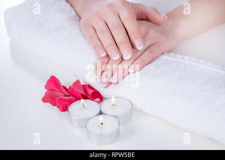 Femme mains avec french manucure style moderne sur serviette avec des pétales de rose rouge et bougie dans un salon de beauté. Manucure et beauté concept. Close up Banque D'Images