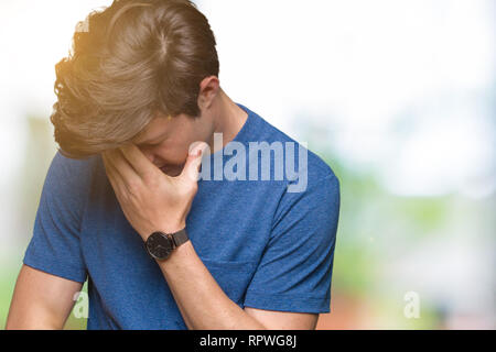 Beau jeune homme portant un tee-shirt bleu sur fond isolé avec expression triste couvrant le visage avec les mains en pleurant. Concept de dépression. Banque D'Images