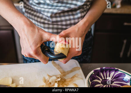 Mains femme de pommes de terre peler. Peelings sur planche à découper en bois Banque D'Images