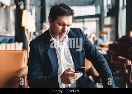 Beau jeune homme assis dans un bar, à l'aide de son téléphone portable pour lire les dernières nouvelles et rester informé. Banque D'Images