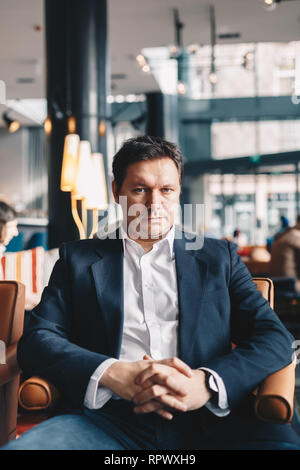 Close-up portrait of young businessman bien à l'estime de soi, assis dans un bar, qui pose pour la caméra. Vertical image avec l'espace pour le texte Banque D'Images