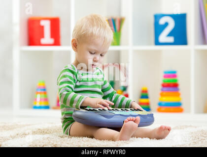 Kid boy joue piano jouet sitting on floor in nursery Banque D'Images