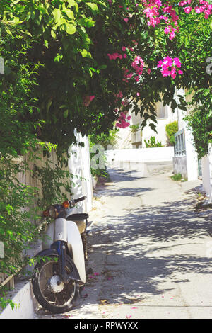 Rues de la ville dans l'île de Poros Neorio, Grèce ; moto garée dans rue étroite couverte de fleurs roses Banque D'Images