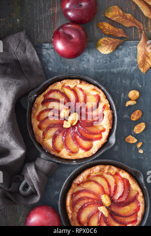 Crumble aux prunes tartes faites maison cuit dans des tranches de petits poêlons en fer. Haut de jeter sur conseil en bois brun foncé avec un peu de pruneau, noix et feuilles rouges Banque D'Images