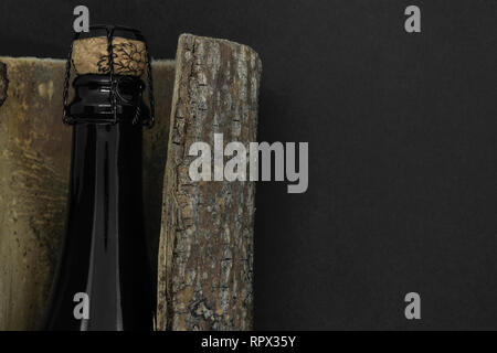 Composition abstraite de champagne cork beige fermé avec bouteille en verre noir placé dans l'écorce des arbres sur fond noir Banque D'Images