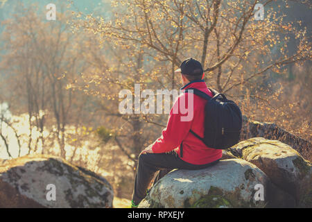 Un touriste est assis sur un rocher au-dessus d'un magnifique canyon sur une journée ensoleillée d'automne. L'homme regarde la rivière Banque D'Images