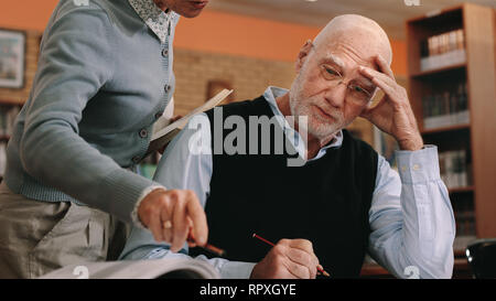 Senior en classe avec la main pour la tête en regardant un livre. Portrait d'un maître de guider un étudiant avancé en classe. Banque D'Images