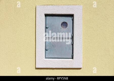 Compteur électrique métal verrouillée en plein air fort avec l'interrupteur montée au mur de la maison avec nouvelle façade entouré avec cadre blanc sur chaude journée ensoleillée Banque D'Images