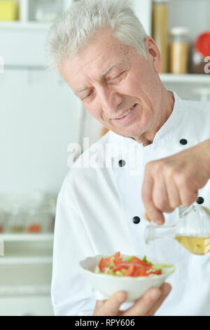 Portrait of elderly male chef versez de l'huile dans la salade Banque D'Images