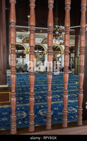 Les hommes observant les prières de midi, Kampung Kling Mosquée, Masjid Kampung Kling, Melaka, Malaisie. Les fusées de style Malaisien sculpté dans la fenêtre. Banque D'Images