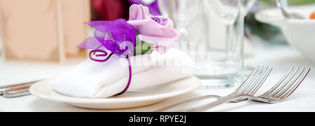 Décoration de table close-up blanc serviette pliée de pourpre violette noeud sur une assiette, verres vides et fourches. Anniversaire de mariage, banquet partie prêt Banque D'Images
