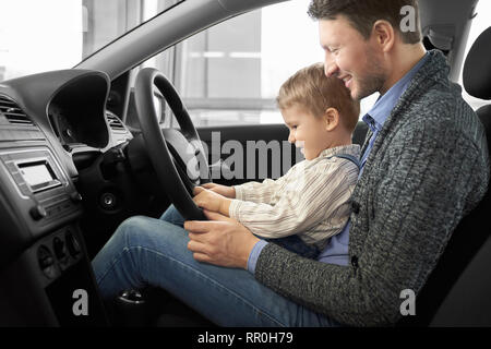 Fils Père tient sur les genoux, l'homme assis dans le siège du conducteur de voiture cher nouveau. Parent montrant à kid location chalet, volant. Famille heureuse l'observation d'automobile, souriant. Banque D'Images