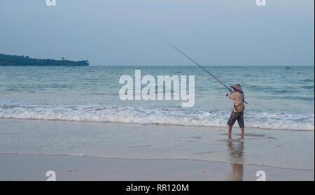 Pêcheur solitaire portant un chapeau conique à l'aide d'une canne de pêche au large de la plage de La Baie de Jimbaran Bali Indonésie. Banque D'Images