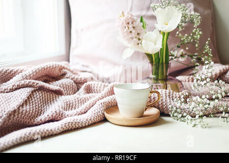 Pâques Printemps confortable, scène de la vie encore. Tasse de café, rose plaid tricoté et bouquet dans un vase sur la fenêtre. Vintage photo style féminin Banque D'Images
