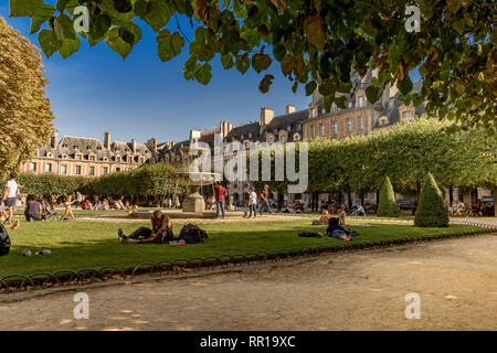 Personnes assises et bains de soleil sur les pelouses près de la fontaine de la place des Vosges , dans le quartier à la mode du Marais de Paris, France Banque D'Images