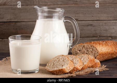 Verseuse et verre de lait avec une miche de pain sur un fond de bois Banque D'Images