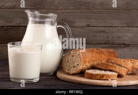 Verseuse et verre de lait avec une miche de pain sur un fond de bois Banque D'Images