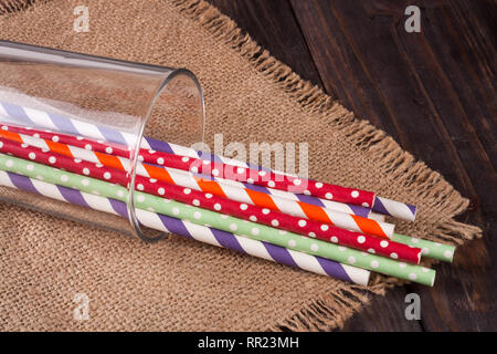 Rayures colorées en verre potable pailles sur une table en bois avec sac Banque D'Images