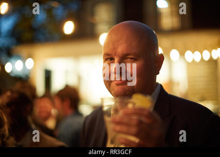 Confiant smiling man toasting avec boisson dans la main dans la nuit Banque D'Images