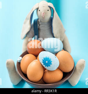 Lapin de Pâques tient dans ses pattes une plaque d'argile brun avec des oeufs de Pâques. Beau fond bleu. Idées de Pâques. L'espace pour le texte. Joyeuses Pâques. Banque D'Images