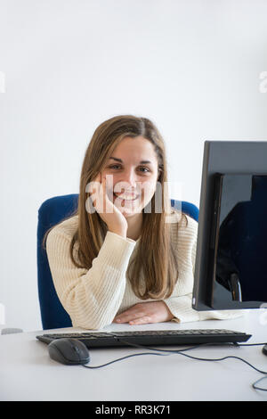Jeune secrétaire souriant au travail dans un bureau blanc devant l'ordinateur. Concept agréable et joyeux de service à la clientèle. Banque D'Images