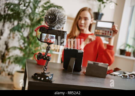 Conseils de beauté. Jeune femme séduisante montrant une palette de maquillage sur l'appareil-photo pendant l'enregistrement vidéo examen pour sa beauté blog. La beauté. Instagram. La diffusion. Banque D'Images