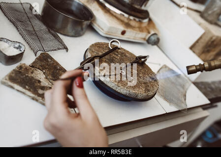 Opération dangereuse. Vue de dessus les mains de bijoutier un soudage avec Silver Earring de flamme d'un chalumeau à l'atelier de fabrication de bijoux. Banque D'Images