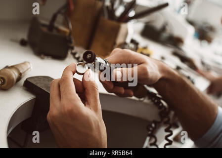 Sur le chemin de la perfection. Close-up of homme bijouterie Bague en argent de polissage les mains à son studio de fabrication de bijoux. Atelier de fabrication de bijoux. Master's hands Banque D'Images