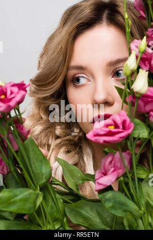 Close up de printemps belle jeune femme se cachant derrière Eustoma fleurs isolé sur gray Banque D'Images