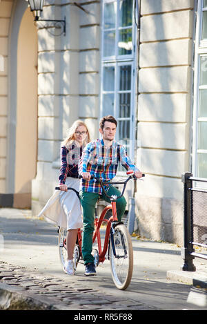 Jeune couple voyageur smiling actif, beau barbu et très jolie jeune femme dans des verres ensemble tandem le long des trottoirs pavés lumineux sur la journée ensoleillée par d'anciens bâtiments. Banque D'Images