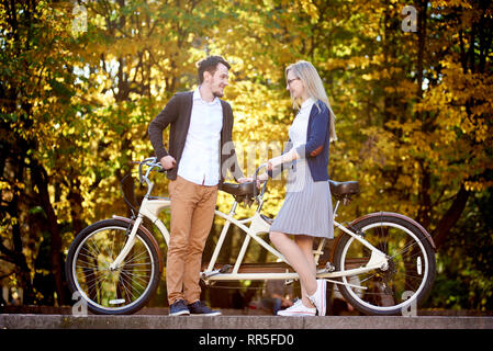 Young happy couple romantique, barbu et jolie femme fermer ensemble au double tandem location à l'extérieur dans le parc ou sur la forêt d'automne lumineux ensoleillé jaune d'arbres à feuillage dense. Banque D'Images