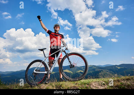 Heureux sportif professionnel permanent cycliste avec cross country location sur une colline, à la collecte, la main contre le ciel bleu avec des nuages sur l'été journée ensoleillée. Sport de plein air, la réussite des objectifs de vie et concept Banque D'Images