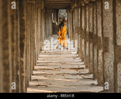 Orange femme vêtue de marcher au milieu de piliers du temple Virupaksha Temple à Hampi en Inde karnakata Banque D'Images