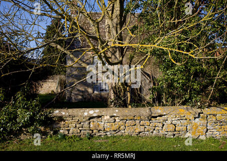Vieille maison en pierre derrière mur de pierre et d'arbres Banque D'Images