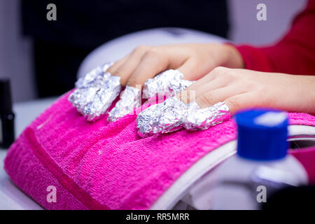 La main de la femme de papier aluminium sur les ongles sur une serviette rose in nail salon. Banque D'Images