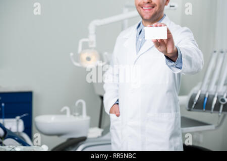 Portrait of cheerful dentiste debout avec la main dans la poche et holding blank card Banque D'Images