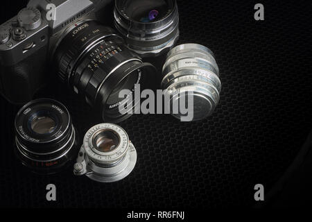 Appareil photo Mirrorless équipé d'un convertisseur optique et une sélection de verres vintage M42 sur un fond noir. Banque D'Images