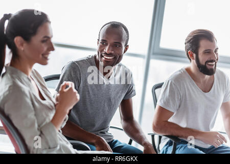 Groupe de rire multiraciale businesspeople talking et plaisantaient assis sur des chaises de bureau moderne, convivial multi-ethnic business te Banque D'Images