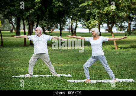 La haute couple practicing warrior II pose en se tenant sur le tapis de yoga Banque D'Images