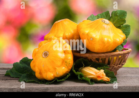 Pattypan avec feuille de courge jaune dans un panier en osier sur fond flou de table en bois Banque D'Images