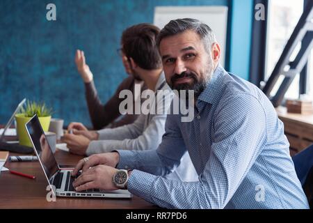 L'âge moyen top manager travaillant à la table en bois dans un design intérieur moderne. Barbu élégant businessman using laptop on workplace Banque D'Images